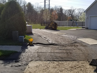 Front of house/driveway picture showing the care taken to protect the driveway and yard during construction of a dark green and grey backyard basketball court in Agawam, MA.