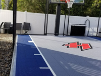 Closeup of blue and grey basketball court surface with custom H logo in Braintree, MA, after finishing landscape and hardscape touches around it were completed.