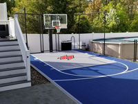 Small blue and grey basketball court with custom red H logo by existing pool in Braintree, MA, shown after completion of associated hardscapes.