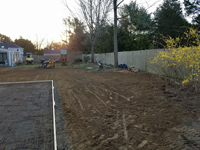 Prep work for construction of dark green basketball court in Duxbury, MA, in context of owner's wider backyard landscaping.