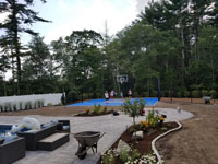 Kids on blue and gray residential basketball court in Easton, MA, with landscaping by Evergreen still in progress.