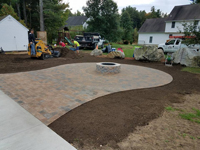 Detail work around partially complete basketball court featuring Celtics logo, with fire pit, patio, and light for night play, in Londonderry, NH.