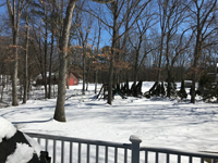 Snow covered before picture of the planned location of a tan and green basketball court in Londonderry, NH, featuring multiple custom logos and writing, lighting for night play, and optional multicourt net for volleyball.