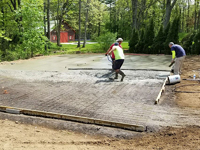 Pouring and leveling cement on compacted surface where a basketball court will be built.