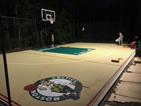 Kids helping to test the lighting adjustments on tan and green basketball court in Londonderry, NH, featuring multiple custom logos and writing, lighting for night play, and optional multicourt net for volleyball.