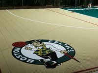 Closeup of custom Celtics logo on corner of sand and green backyard basketball multicourt in Londonderry, NH.