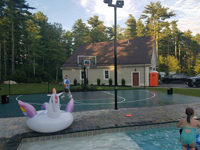 Green and black backyard basketball court adjacent to a pool in Marion, MA, following the finishing landscape touches.