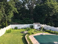 Before picture of poorly drained, scruffy part of yard before construction of royal blue and yellow basketball court and accessories in Stoneham, MA, as seen from a distance adjacent to covered pool.