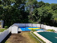 Royal blue and yellow basketball court and accessories in Stoneham, MA, viewed from a distance, adjacent to covered pool.