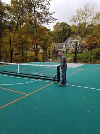Demonstrating deployment of portable yet durable net system to center of large basketball multicourt in Bolton, MA. Court was ordered with lined for pickleball. Portable nets roll easily then lock down, giving option of net sports like tennis on demand without permanent posts or nets. Shown here in final position.