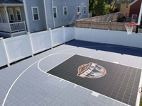 Angled view from back and right end of court towrd house, showing residential basketball court in titanium and blck with custom logo in Boston, MA.