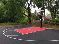 View from front right corner toward back left corner of black and red backyard basketball court in Brockton, MA.