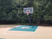 Sand and green colored backyard basketball court with custom Celtics logo in Brockton, MA.