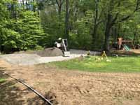 Home basketball court in subdued slate green and burgundy on asphalt in Connecticut. Shown here putting in an underlay that includes packed, crushed stone to make the asphalt under the court more durable.