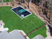 View from above, after landscaping is completed,  of a black and green backyard basketball court in Canton, MA, featuring a custom logo.