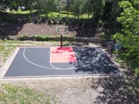 Low level drone shot from front to back of black and red backyard basketball court in Dedham, MA.