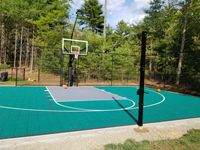 Optional post to enable a net across court for games like tennis, volleyball and pickleball, with adjustable height, on backyard basketball court in Dover, MA.