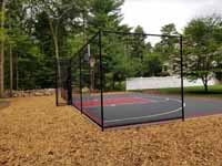Completed Middleboro, MA backyard court viewed from rear of left side, through containment fence and showing off the landscape around it.