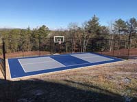 Multicourt for pickleball and basketball, fenced on three sides, on a hillside backyard in Plymouth, MA. View after construction completed.