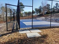 Multicourt for pickleball and basketball, fenced on three sides, on a hillside backyard in Plymouth, MA.