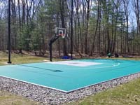 View of finished backyard basketball court from same angle as asphalt base. The tall posts on either side of the hoop are a lighting system for night play in Reading, MA.