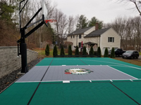 Side view down green and titanium backyard basketball court with custom Celtics logo in Upton, MA.