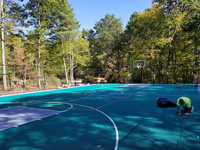 Installation largely complete of ergonomic, low-impact tiles that form the final surface of a large emerald green and titanium backyard basketball court in Bolton, MA.